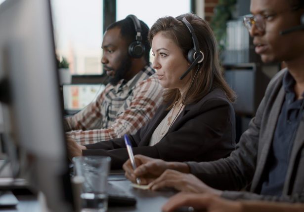 Young woman using audio headset and computer at call center job, offering helpline assistance to people. Female consultant talking to clients at customer care service, helping with telemarketing.